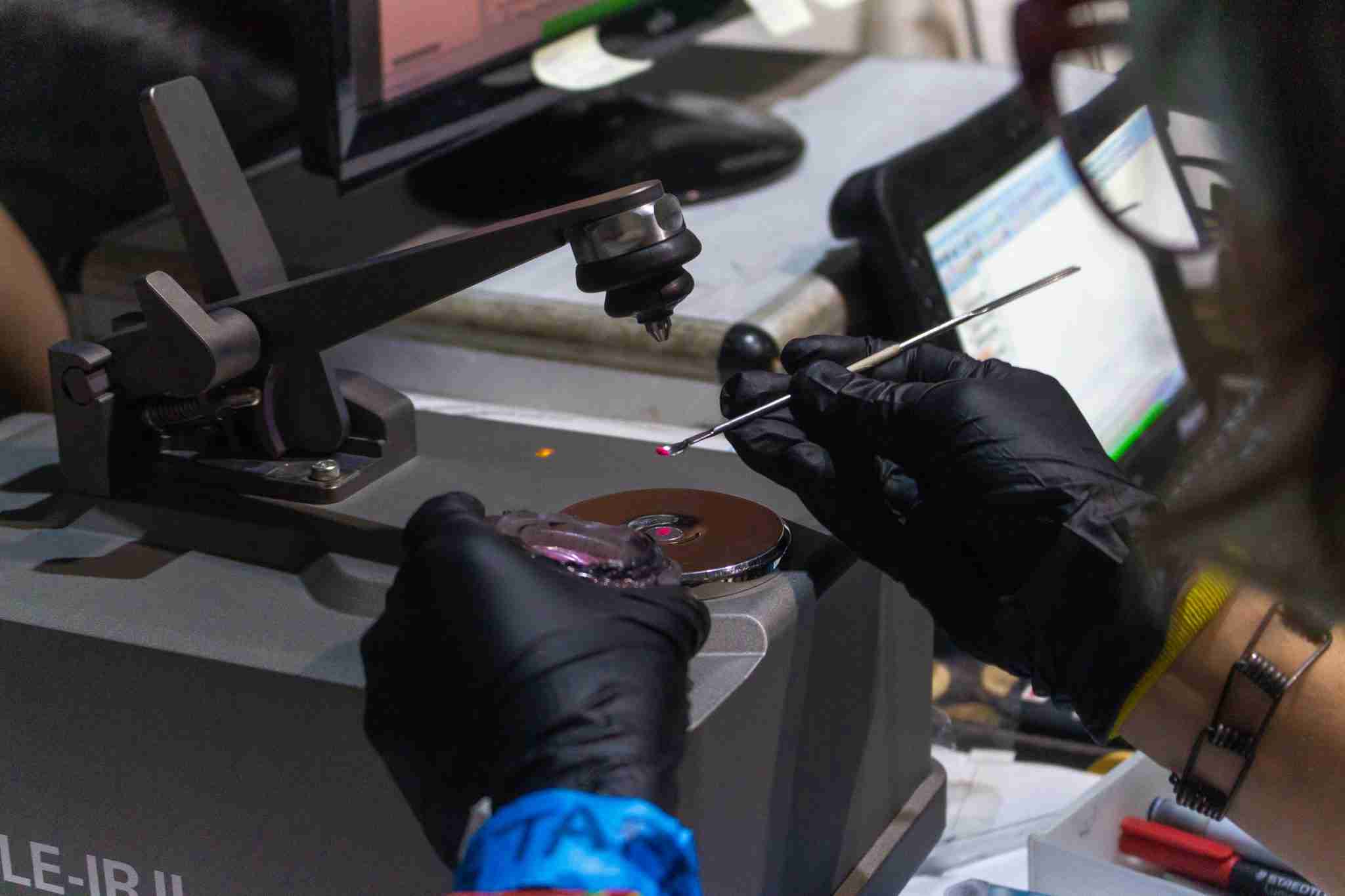 FT-IR En la imagen se observa un proceso de análisis de una muestra utilizando la técnica de espectroscopía infrarroja transformada de Fourier (FT-IR). Un técnico, con guantes negros, manipula una pequeña muestra sobre una plataforma reflectante del dispositivo FT-IR. El entorno muestra equipos tecnológicos, incluyendo una pantalla de computadora en el fondo, donde se procesan los resultados del análisis.